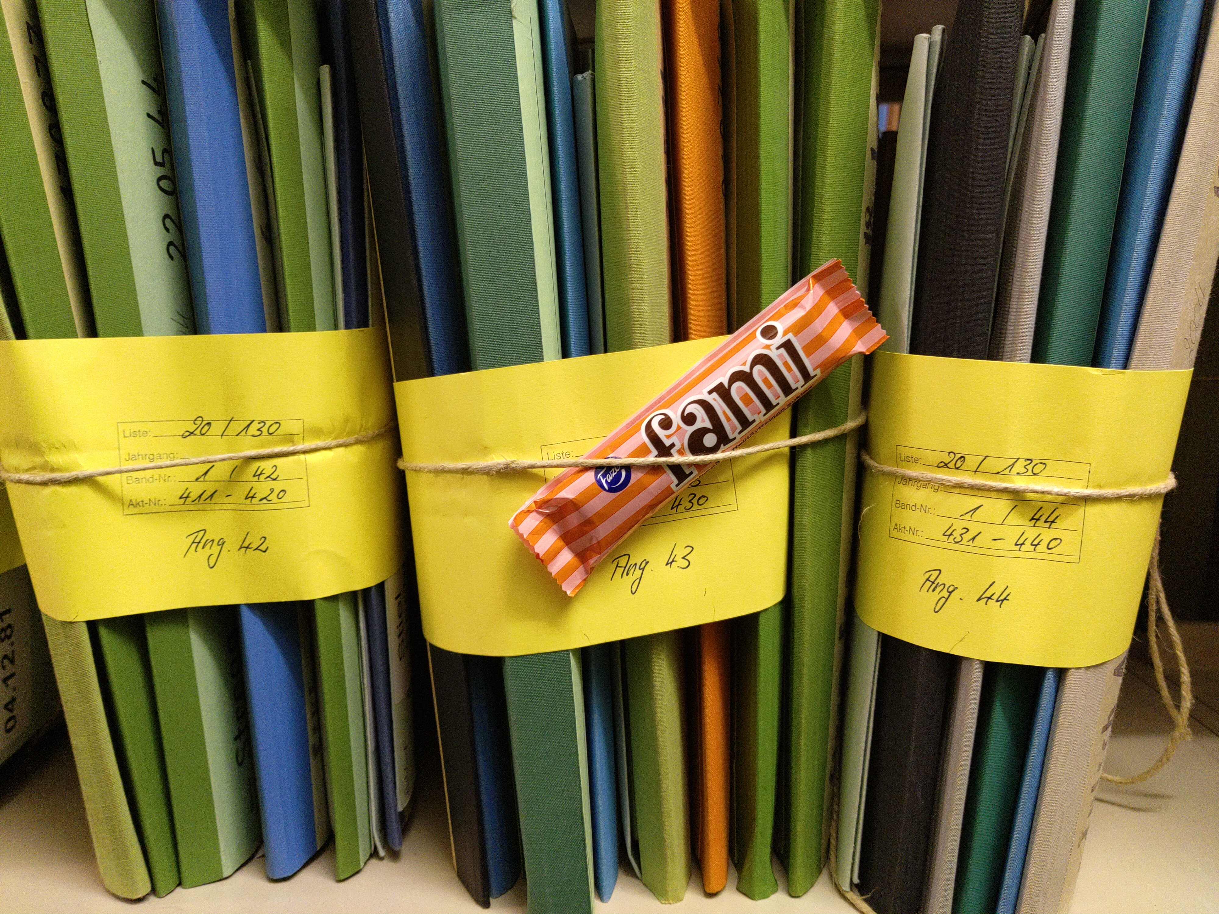 Drei Bündel Archivakten, daran befestigt ein Schokoriegel mit Aufschrift Fami