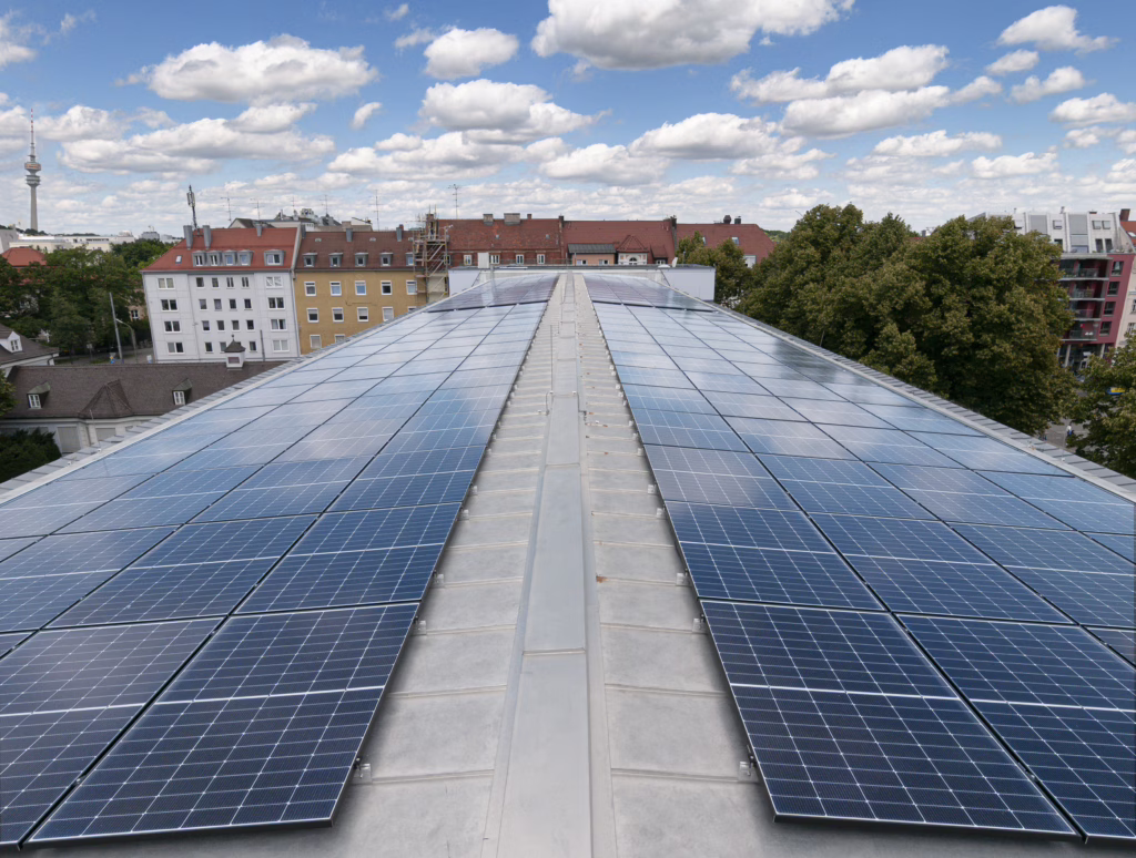 Blick über das Dach mit Photovoltaik-Platten, im Hintergrund der Olympiaturm